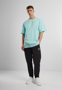 T-shirt rayé bleu clair à manches courtes, associé à un pantalon de survêtement noir avec un logo et des baskets blanches. Design simple et coupe décontractée.