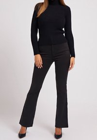 Musta neulottu pooloneule, jossa on vartalonmyötäinen leikkaus ja levenevät mustat housut. Sileä tekstuuri, pitkät hihat ja hillitty ribbineuloskuvio.