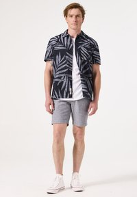 Camisa de manga corta azul marino con patrones de hojas grises, combinada con pantalones cortos gris claro. Zapatillas blancas completan el atuendo.