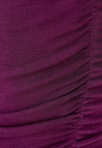 Tissu texturé violet avec des détails froncés, mettant en valeur une finition douce et un subtil éclat, soulignant l'élasticité et la fluidité du tissu.