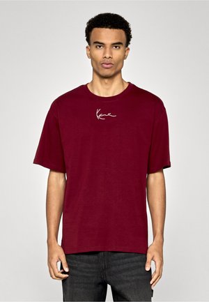 Bordeaux T-shirt i bomull med korta ärmar, med en vit kursiv logotyp på bröstet och en avslappnad passform. Kombineras med mörka jeans.