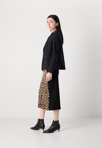 Blazer navy con tasche, abbinato a una gonna al ginocchio con stampa leopardata e tessuto nero. Stivaletti neri con punta a stiletto.