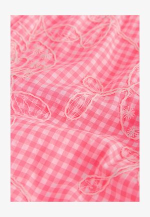 Rózsaszín kockás anyag hímzett virágmintákkal. A textúra sima, látható varrással és a minták körüli fodros részletekkel.