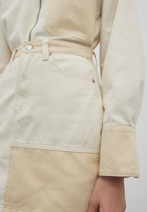 Jumpsuit beige e crema realizzato in cotone, con chiusura con zip, design a pannelli e dettaglio con bottone in vita. Maniche lunghe con polsini.