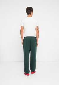 White t-shirt view from the back, paired with dark green joggers featuring a back pocket, and red sneakers with white soles.