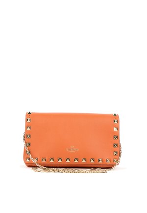 Pochette Valentino orange avec des clous pyramidaux dorés le long des bords et une bandoulière chaîne dorée sur fond blanc.