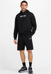 Felpa nera con la scritta "JUST do IT" in bianco, abbinata a pantaloni shorts neri con tasca laterale e scarpe da ginnastica nere e viola.