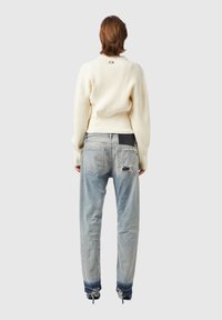 Suéter de canalé crema con mangas anchas, combinado con jeans desgastados de un azul claro que presentan un dobladillo deshilachado y un solo agujero en el bolsillo trasero.