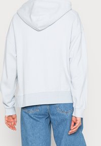 Sudadera con capucha de color azul claro, con un corte relajado, hombros caídos, ribete en el dobladillo y puños, fabricada en tela suave, combinada con jeans azules.