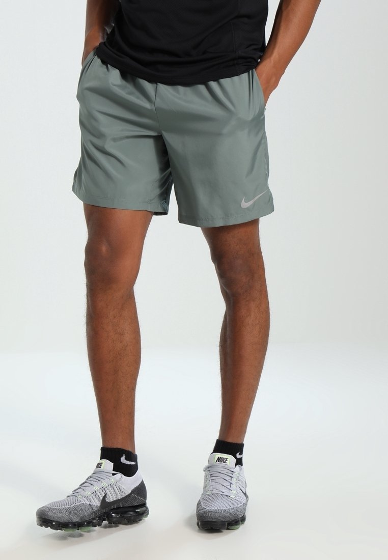 Šedé sportovní šortky s hladkou texturou a elastickým pasem, s malým logem Nike na levé noze. V kombinaci se šedými a černými teniskami.