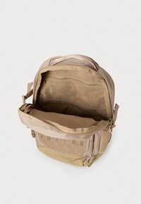 Mochila bege com um interior espaçoso, bolsos em malha e compartimentos com fecho. Possui alças ajustáveis e um tecido durável.