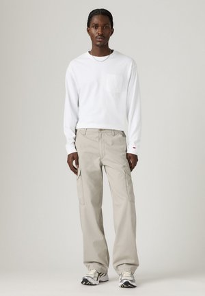 White long-sleeve shirt with a chest pocket, paired with light beige cargo pants featuring side pockets, and patterned athletic shoes.