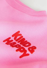 Rosa Baumwoll-Sweatshirt mit auffälligem, rotem Schriftzug "KIND & HAPPY". Der Halsausschnitt ist gerippt und sorgt für eine enganliegende Passform.