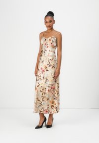 Blommig satinklänning i creme med intrikata mönster av rosa och blå blommor, med tunna axelband och en figursydd bodice; bärs med svarta klackar.