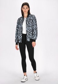 Lyseblå og sort leopardmønstret bomberjakke med ribbede manchetter, båret over en hvid top og parret med sorte leggings og hvide sneakers.