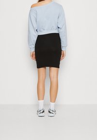Sudadera cortada de color azul claro con mangas largas y un dobladillo acanalado, combinada con una falda ajustada negra. Calcetines blancos y zapatillas grises completan el look.