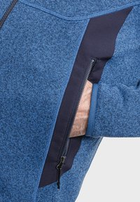 Blaue Fleecejacke aus strukturiertem Material, mit kontrastierenden dunkelblauen Seitenpaneelen und einer Reißverschlusstasche. Verfügt über einen hohen Kragen und eng anliegende Bündchen.