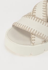 Lys beige åpen tå sandal med tykk såle, sydd detaljer langs stropper, og en glatt lær finish. Kontrasterende tråd detaljer.