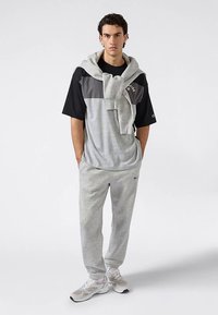 Camiseta de manga corta en bloques de color gris y negro con pantalones deportivos gris claro, con una sudadera con capucha colgada alrededor del cuello.