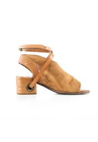 Sandale ouverte en daim beige avec talon carré bas, bride à la cheville et sangle diagonale en cuir reliant le talon à la fermeture de la cheville.
