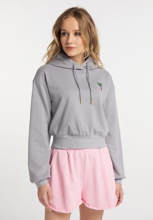Grijze cropped hoodie met trekkoorden en een klein groen en bruine palmboom ontwerp. Gecombineerd met lichtroze sportshorts met een gebogen zoom.