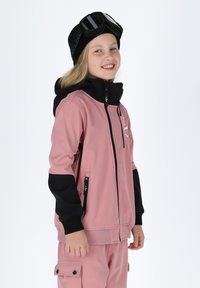 Lyserød og sort softshell-jakke med lynlåslommer, ribbede manchetter og høj krave, iført med matchende bukser og en sort strikhue.