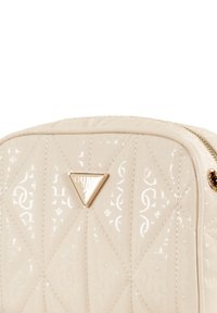 Borsa trapuntata beige con finitura lucida, caratterizzata da un accento dorato a forma triangolare. Chiusura con zip e trama a rombi.