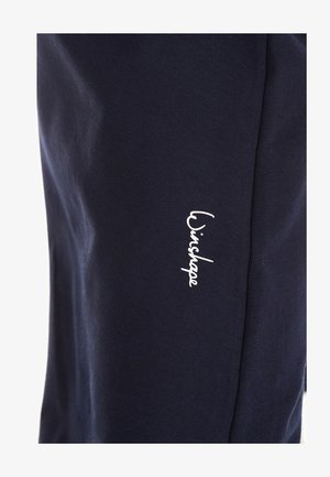 Námorné joggers s mäkkým bavlněným materiálom, úzkym strihom a bielym logom na ľavom stehne. Hladká textura bez vzorov.