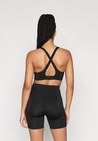 Czarny sportowy biustonosz z krzyżującymi się paskami na plecach, z otwartym tyłem i regulowanym zapięciem na haczyk. Połączony z czarnymi, wysokim stanem szortami.
