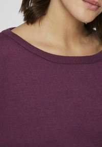Pull en tricot violet avec un large col et une texture douce, montré du col jusqu'à l'épaule.