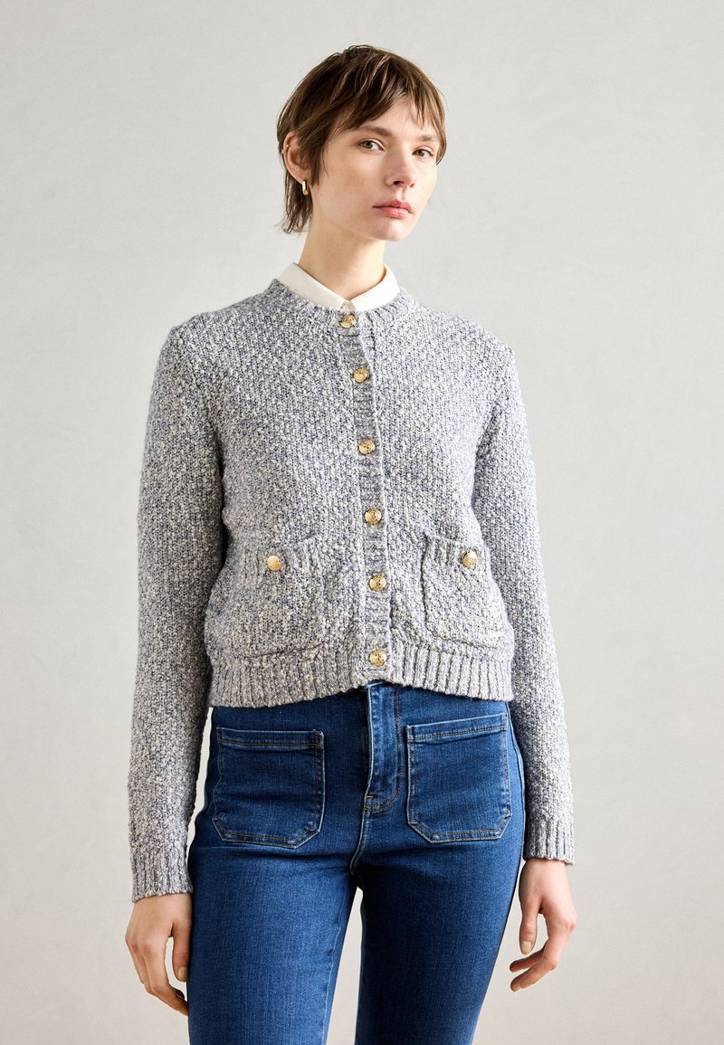 Gray textured cardigan with a round neck, gold buttons, and two front pockets. Worn over blue high-waisted jeans.