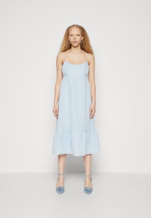 Light blue midi dress with textured fabric, thin straps, fitted bodice, and flared hem. Accompanied by matching blue heeled shoes.