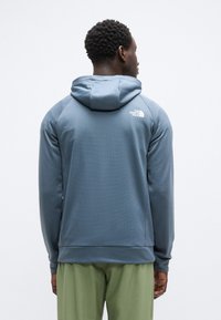 Ανδρικό μπλε φούτερ με κουκούλα από υφασμάτινο υλικό με υφή, που διαθέτει κουκούλα και ένα μικρό λευκό λογότυπο στην πλάτη. Εφαρμοστή σχεδίαση με απλή φινέτσα.