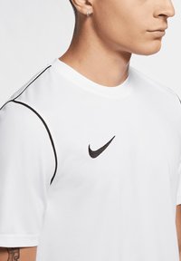 T-shirt sportivo bianco realizzato in tessuto morbido, con dettagli neri lungo le maniche e un piccolo logo Nike nero sul petto.