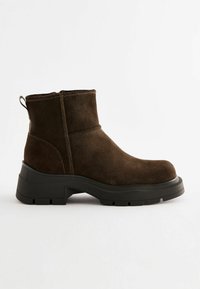 Bottines en daim marron avec une semelle en caoutchouc noir épaisse, dotées d'une languette à l'arrière et de subtils détails de couture.