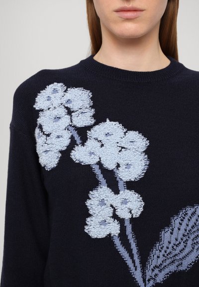 Navy knit sweater featuring a textured light blue floral design with raised stitching. Round neckline and long sleeves.