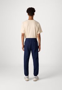 Tricou din bumbac bej și pantaloni jogger cu talie elastică bleumarin, cu un buzunar pe spate, asortați cu adidași gri și bej. Design minimalist, croială lejeră.