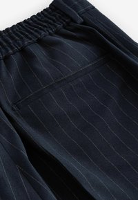 Navy striped trousers featuring a gathered waistband, soft texture, and a single back pocket with contrasting stitching detail.