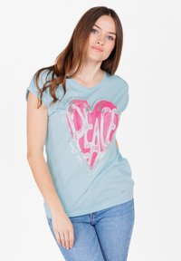 Camiseta de color azul claro con mangas cortas, que presenta un gráfico de un corazón rosa con la palabra "PAZ" en letras grandes. Tela de algodón suave.