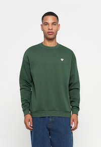 Felpa verde in cotone con scollo rotondo, polsini e orlo a coste. Presenta un piccolo logo ricamato sul petto.
