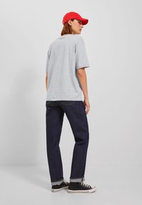 Grå T-skjorte, løs passform, kombinert med mørkeblå jeans med oppbrettede mansjetter og svarte høye sneakers. Rødt caps vendt bakover gir en fargekontrast.