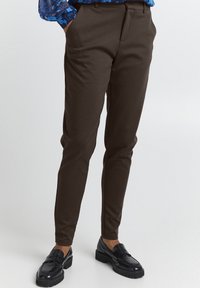 Bruna skräddarsydda byxor med smal passform, tillverkade av mjukt tyg. Har en platt front och sidofickor. I kombination med glänsande svarta loafers.