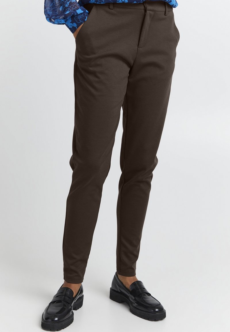 Bruna skräddarsydda byxor med smal passform, tillverkade av mjukt tyg. Har en platt front och sidofickor. I kombination med glänsande svarta loafers.