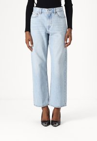 Jeans de mezclilla de tiro alto y pierna ancha en azul claro, con bolsillos frontales y un ligero desvanecimiento. Combinados con tacones negros.