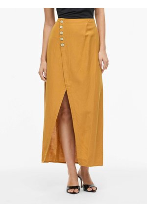 Jupe portefeuille jaune moutarde avec cinq boutons sur le côté, fente avant révélant une jambe, portée avec des talons noirs ouverts à l'avant et un haut noir.