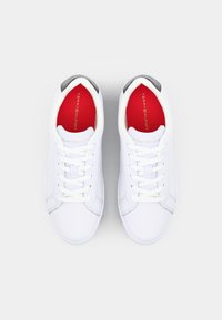 Białe trampki z gładką skórzaną cholewką, z szarymi akcentami na pięcie, białymi sznurowadłami oraz żywo czerwonym wkładką z logo.