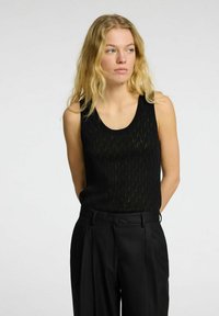 Black sleeveless top with a textured wave pattern, made from lightweight fabric. Paired with high-waisted black trousers.