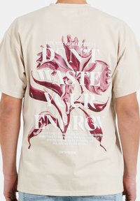 Camiseta de algodón beige con un gran gráfico floral en color burdeos y texto blanco en la parte posterior, que presenta la frase "NO DESPERDICIES TU ENERGÍA."