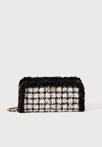 Black and white checkered tweed handbag with textured black trim, gold logo accent, and a detachable chain strap. Rectangular shape.