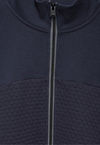 Chaqueta navy de cremallera con un panel inferior texturizado, cuello de canalé y cremallera en contraste con un acento a rayas. Acabado de tejido suave.